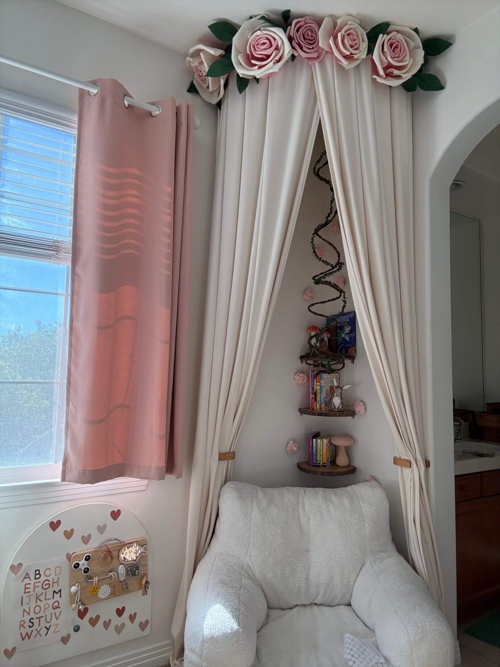 Cozy corner with a white armchair, beige curtains, and soft pink drapes by a sunlit window.