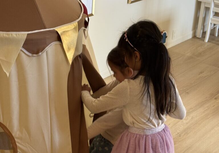 A young girl playing inside a beige fabric tent indoors.